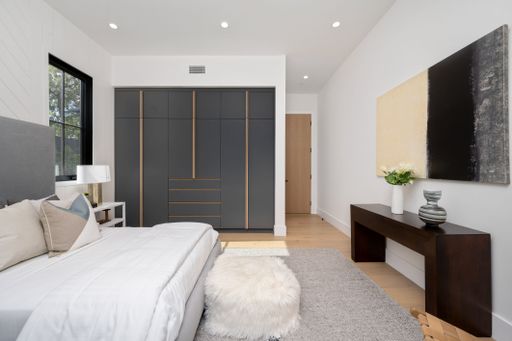 Modern bedroom interior with a large bed, stylish black wardrobe, and contemporary decor.