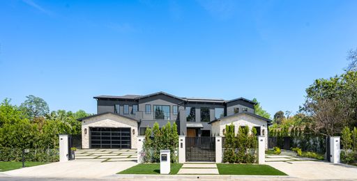 Modern luxury house with a large driveway and lush greenery under a clear blue sky.