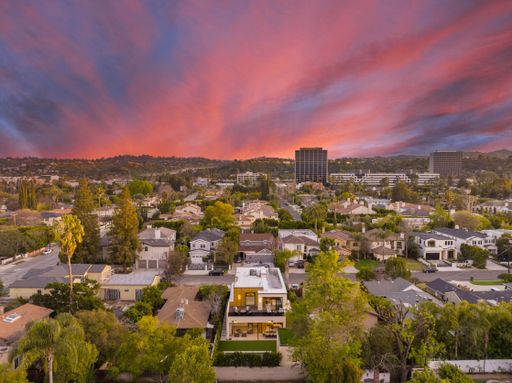 Aerial view of a suburban neighborhood with a vibrant sunset sky, featuring residential houses and distant office buildings.