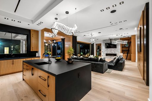 Modern open-plan kitchen and living room with sleek wooden cabinetry, black countertops, and stylish lighting fixtures.