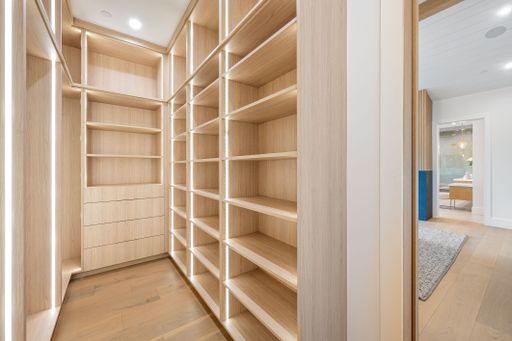 Modern wooden walk-in closet with ample shelving and drawers, illuminated by recessed lighting, in a contemporary home interior.