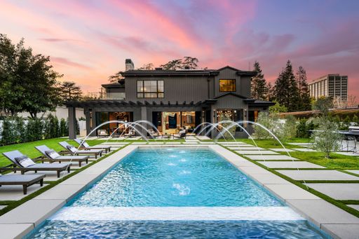 Modern luxury home with a swimming pool, sun loungers, and a beautiful sunset sky.
