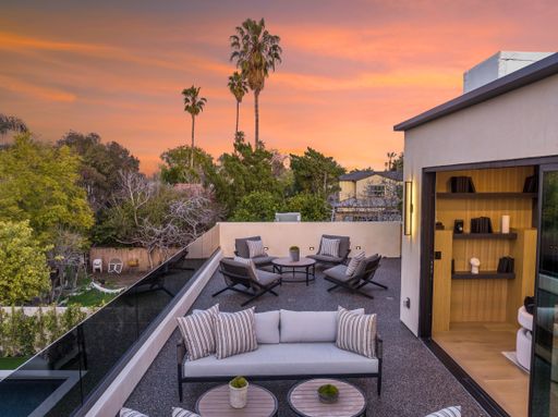 Modern rooftop patio with outdoor furniture and a beautiful sunset view, surrounded by trees and palm trees.