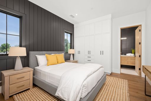 Modern bedroom with black paneled walls, white bedding, and yellow pillows, featuring wooden furniture and a view into a sleek bathroom.