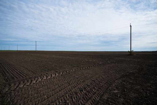 A landscape of plowed brownfield with electric posts background under a cloudy sky