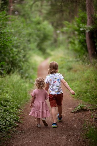 A selective of a young boy walking in the forest with his little sister
