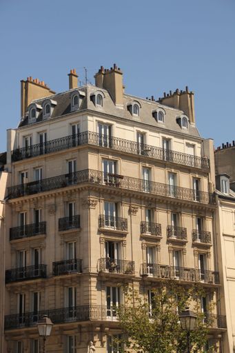 A classic Parisian apartment building with wrought iron balconies against a clear blue sky.