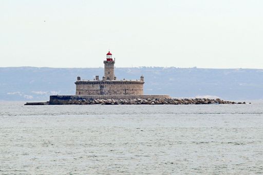 A solitary lighthouse standing on a rocky breakwater in the middle of the sea with distant hills in the background