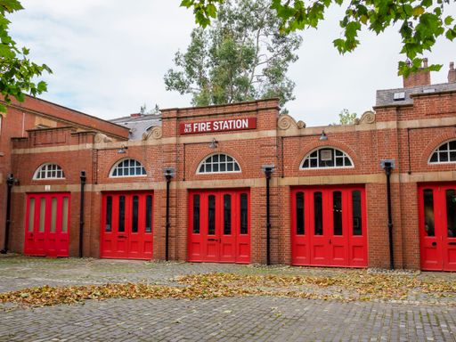 Salford, Manchester, UK. September, 28, 2024: Historic brick fire station with red doors and arched windows on a calm, leafy day.