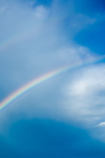 A vertical closeup shot of a beautiful rainbow in the blue sky