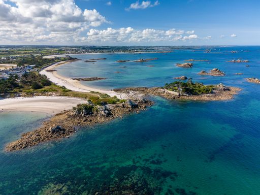 A stunning aerial view of a coastal landscape with clear blue waters, sandy beaches, and rocky islets under a bright sky.