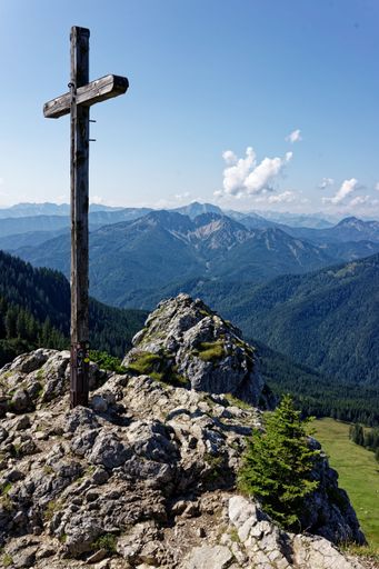 A vertical shot of a wooden cross on top of a hill in Mangfall Mountains, Bavarian Prealps, Southern Germany