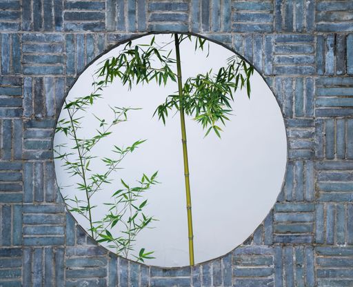 A serene view of bamboo plants through a circular opening in a brick wall, showcasing a blend of nature and architecture.