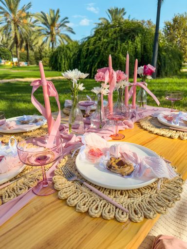A picnic table by the river adorned with candles and pink tableware for a birthday celebration.