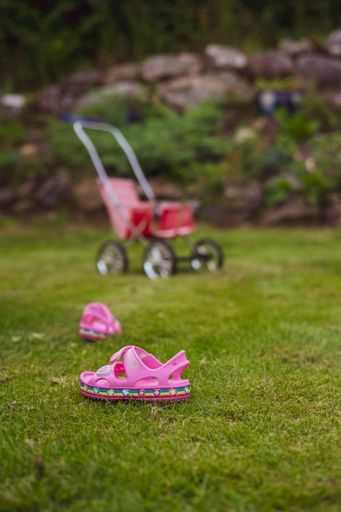 A vertical shot of pink baby sandals on the grass and a stroller in the background