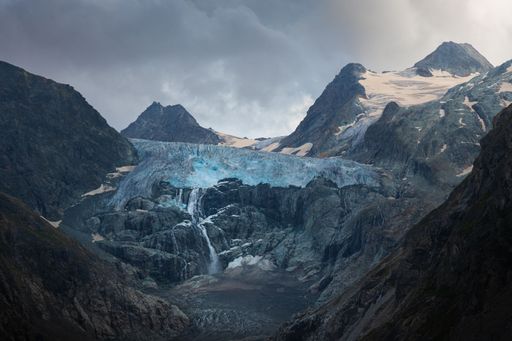 A scenic view of a melting Swiss glacier surrounded by dark clouds at sunset