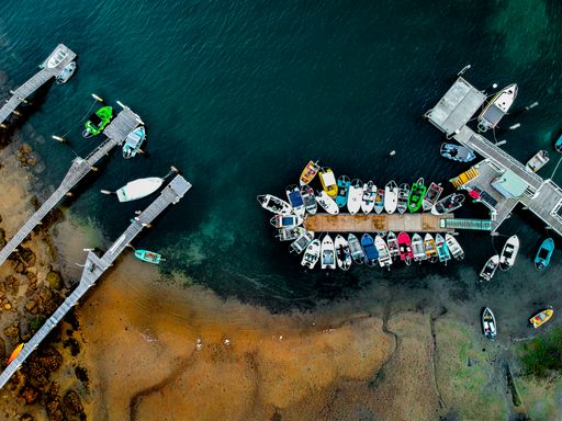 an aerial view of boats moored along the jetty and sandy shore with green water