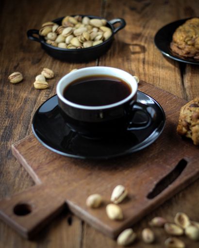 A vertical shot of coffee on a wooden cutting board with pistachios and a biscuit
