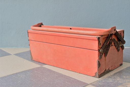 Rusty old red toolbox closed and against a grey background