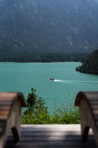 A vertical shot of a beautiful landscape with lake in the mountains and a ship seen from high deck