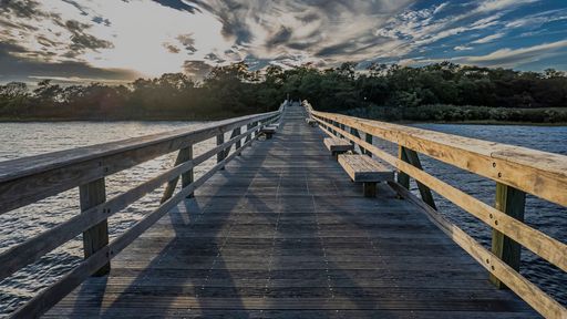 A low angle view of a long wooden pier on a sunny day with clouds in the blue sky.