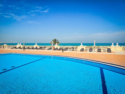 A luxurious swimming pool area with lounge chairs overlooking the ocean under a clear blue sky.
