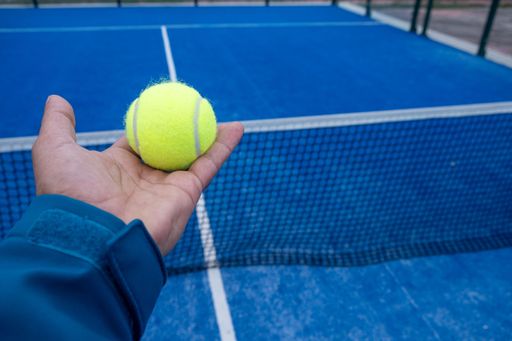man's hand holding a ball on a padel tennis court