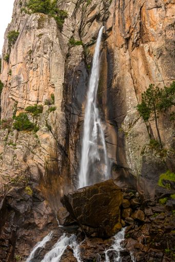 A vertical shot of a waterfall on a cliff with lush trees around it in Corsica, France
