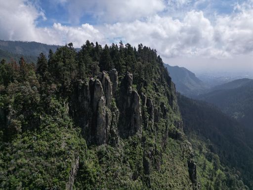 Aerial view of a lush green mountain ridge with rocky outcrops and a cloudy sky.