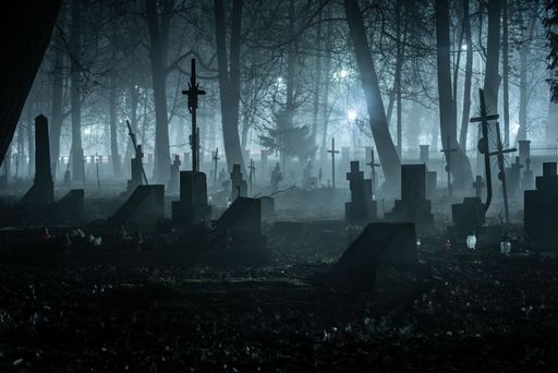 A foggy cemetery at night with silhouettes of tombstones and trees creating an eerie atmosphere