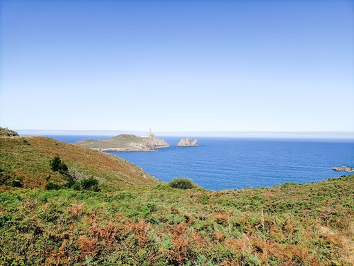 A stunning coastal landscape featuring a rocky island with a lighthouse, surrounded by the blue sea under a clear sky.