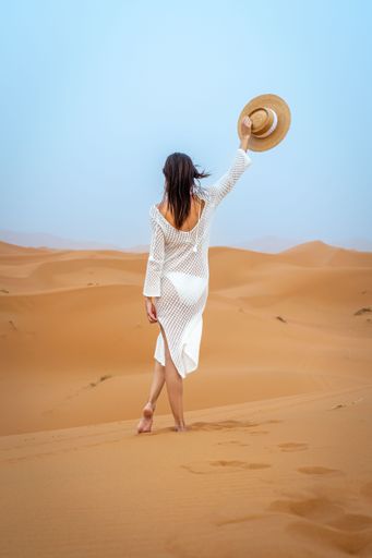 A woman in a white dress and hat walking in the desert with clear blue sky. The image captures the serene beauty of the desert landscape.