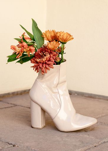 A unique still life of a beige high-heeled boot filled with vibrant flowers, set against a neutral background.