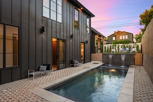 A modern backyard with a sleek pool and water features at sunset. Southern California