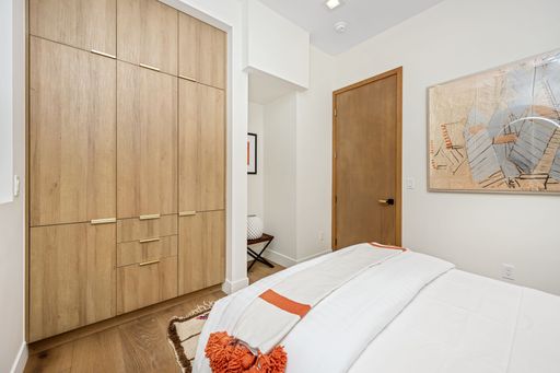A modern bedroom with wooden wardrobe, abstract art, and cozy bedding in neutral tones
