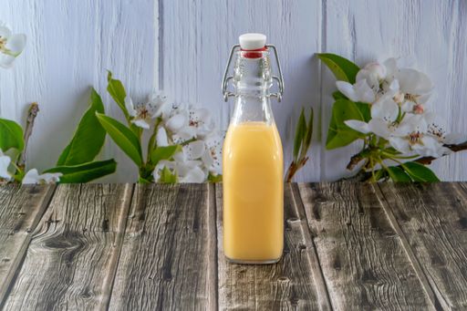 A selective focus shot of an orange drink in a glass bottle on a wooden table with apple flowers