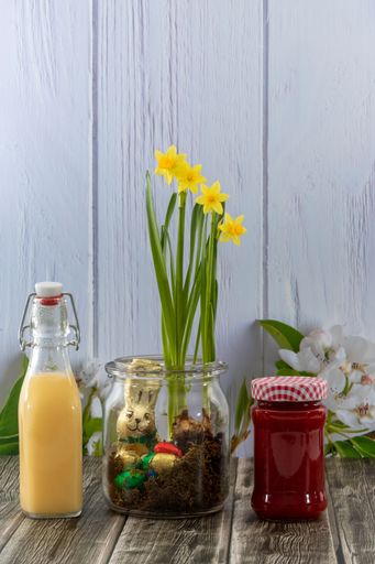 A vertical shot of daffodils and Easter candies in a jar on a table with juice and jam