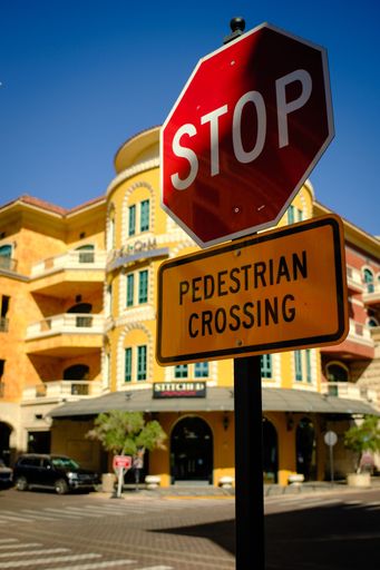 An urban street scene with a stop and pedestrian crossing sign in front of a colorful building
