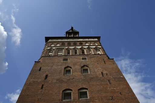 Low angle view of a historic brick tower against a clear blue sky with clouds, showcasing architectural details.
