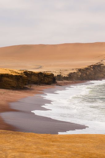 A coastal landscape with cliffs and waves crashing on a sandy beach in Paracas National Reserve, Peru