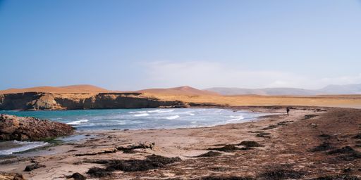 Scenic view of a deserted beach with rocky cliffs and waves under a clear blue sky in Paracas, Peru.