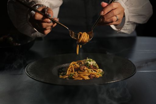 Close-up of a person twirling pasta with a fork and spoon on a dark plate, emphasizing culinary elegance and gourmet dining.