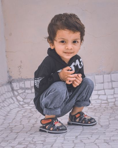 A closeup shot of a little kid boy sitting on the ground and looking at the camera