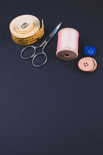 A flat lay of scissors, measuring tape, buttons, and thread on a dark background with free space for text