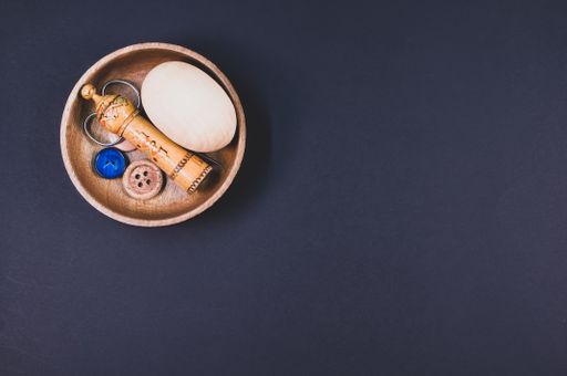 A set of sewing tools inside a wooden bowl isolated on a dark background with free space for text