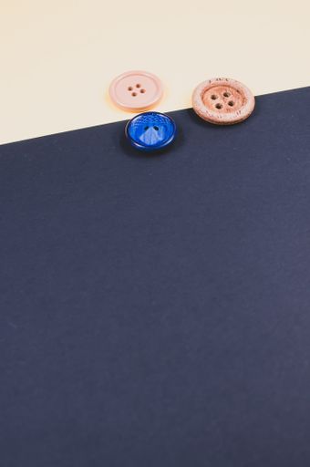 A flat lay of different sizes of sewing buttons on a beige and dark background
