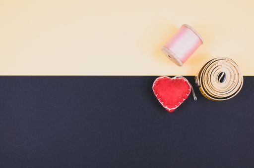 A flat lay of measuring tape, thread, and cushion on a beige and dark background with free space for text