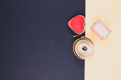 A flat lay of measuring tape, thread, and cushion on a beige and dark background with free space for text