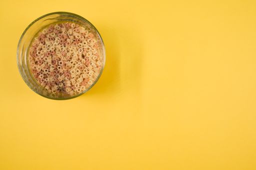 A glass of macaroni pasta on a yellow background with free space for text