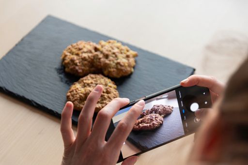 A woman taking a picture of homemade cookies on a wooden board in her kitchen with her phone